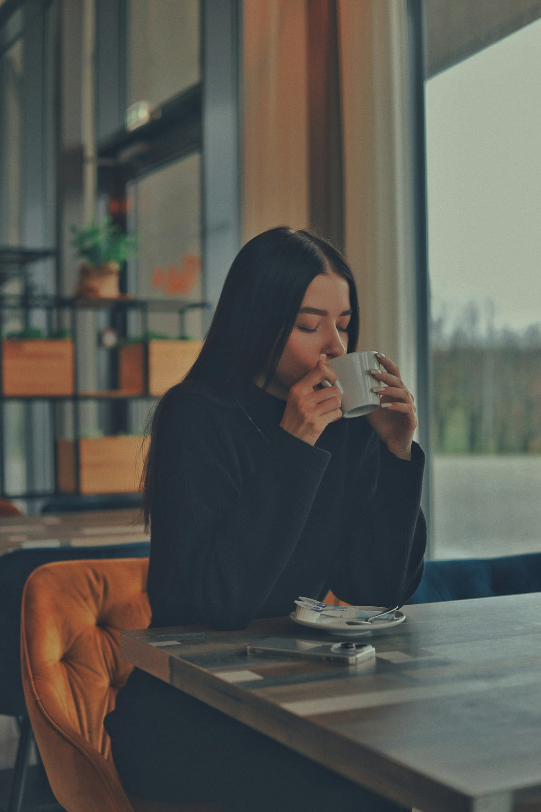 Junge Frau sitzt am Tisch und trinkt eine Tasse Kaffee
