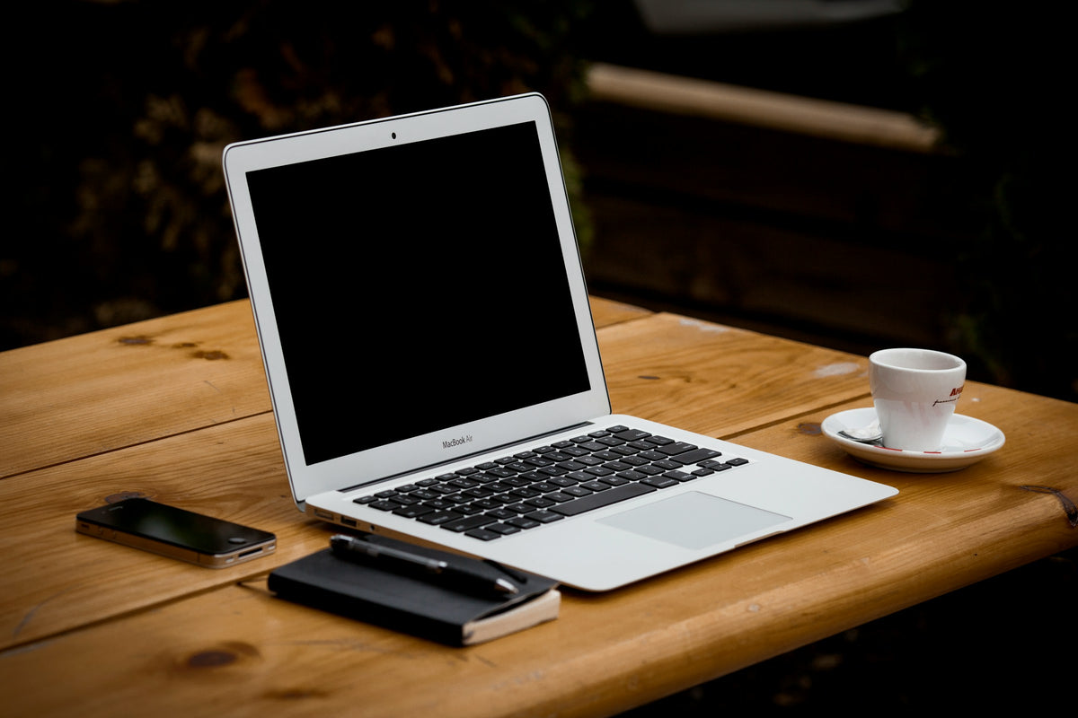 Laptop mit Kaffeetasse und Handy und Notizbuch