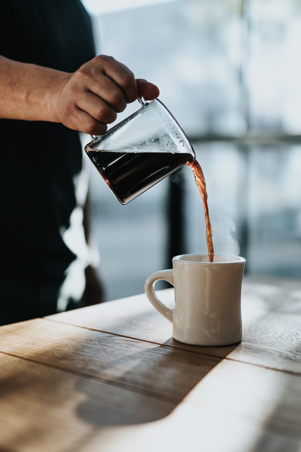 Person schenkt Kaffee in einen Becher ein